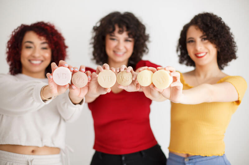Three women wearing different color of shirt holding Vida Bar soap