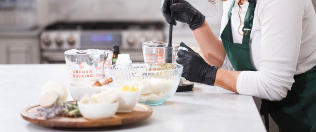 Woman wearing green apron and black gloves mixing ingredients