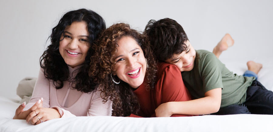 Curly mother smiling wearing red shirt with her daugher and son hugging to her